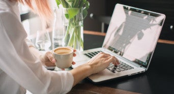 A woman drinking coffee and using a laptop