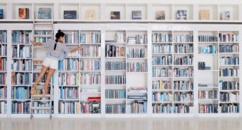 Symbolbild: eine junge Frau durchsucht eine Bibliothek bei ihrer Keyword-Recherche