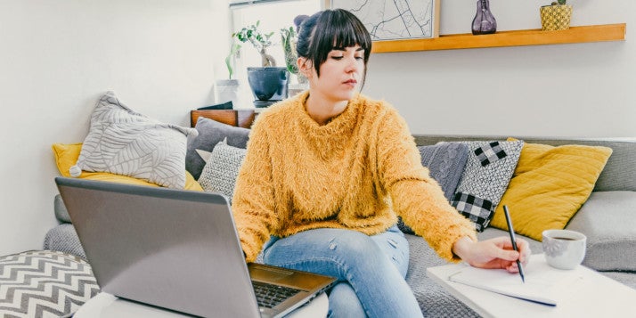Eine Unternehmerin sitzt an ihrem Laptop und notiert sich auf einem Block Ideen für ihr Marketing zu Corona.