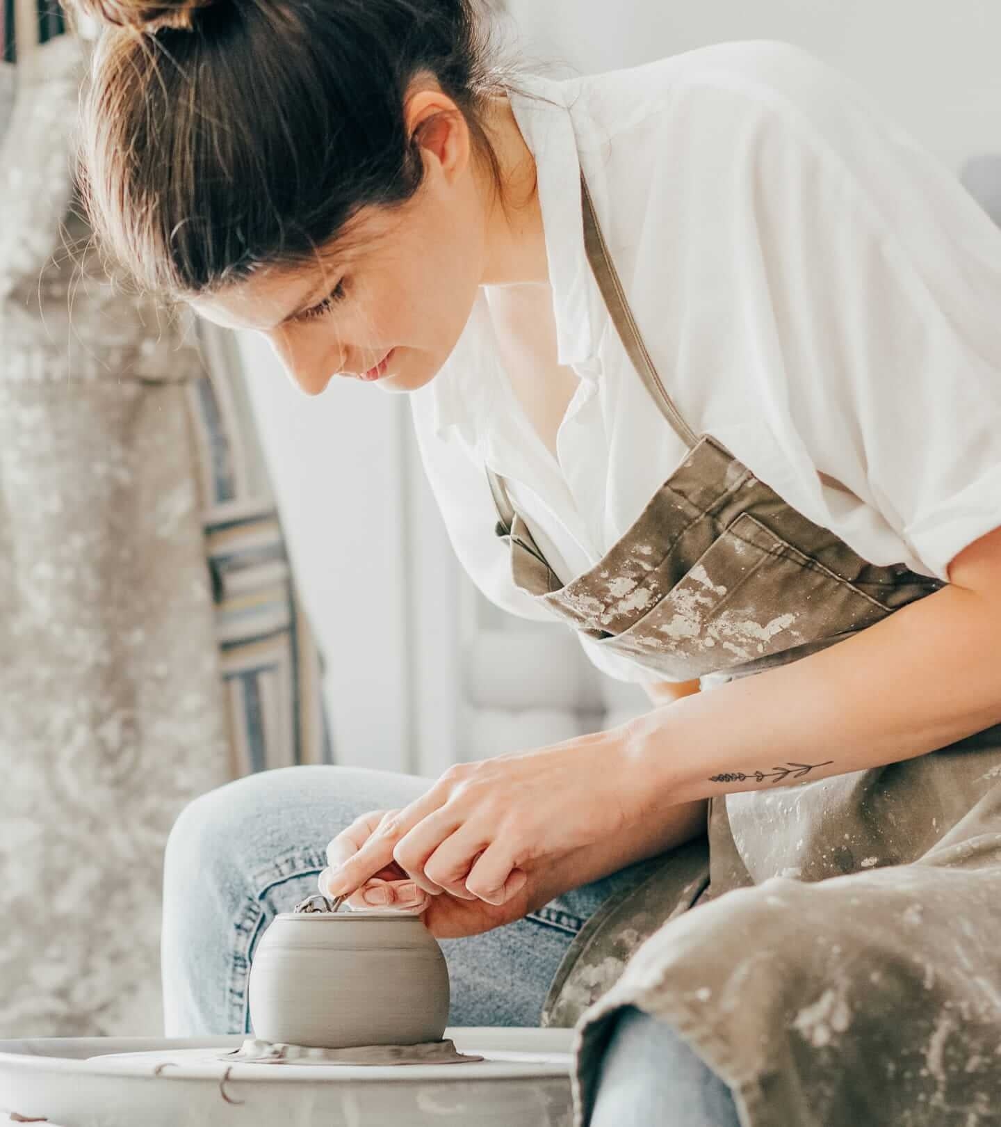 A female potter in overalls forming clay pottery to sell on her online store.