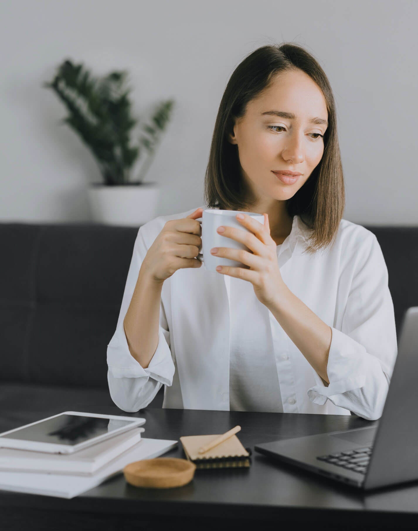 Une femme boit un café et regarde son CV en ligne sur un ordinateur portable.