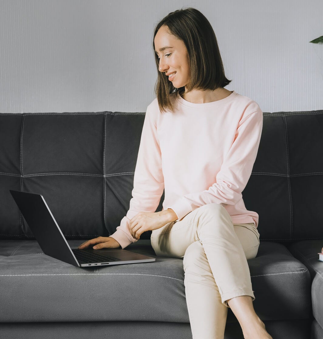 Une femme assise sur un canapé travaille à la création de son CV en ligne sur son ordinateur portable.